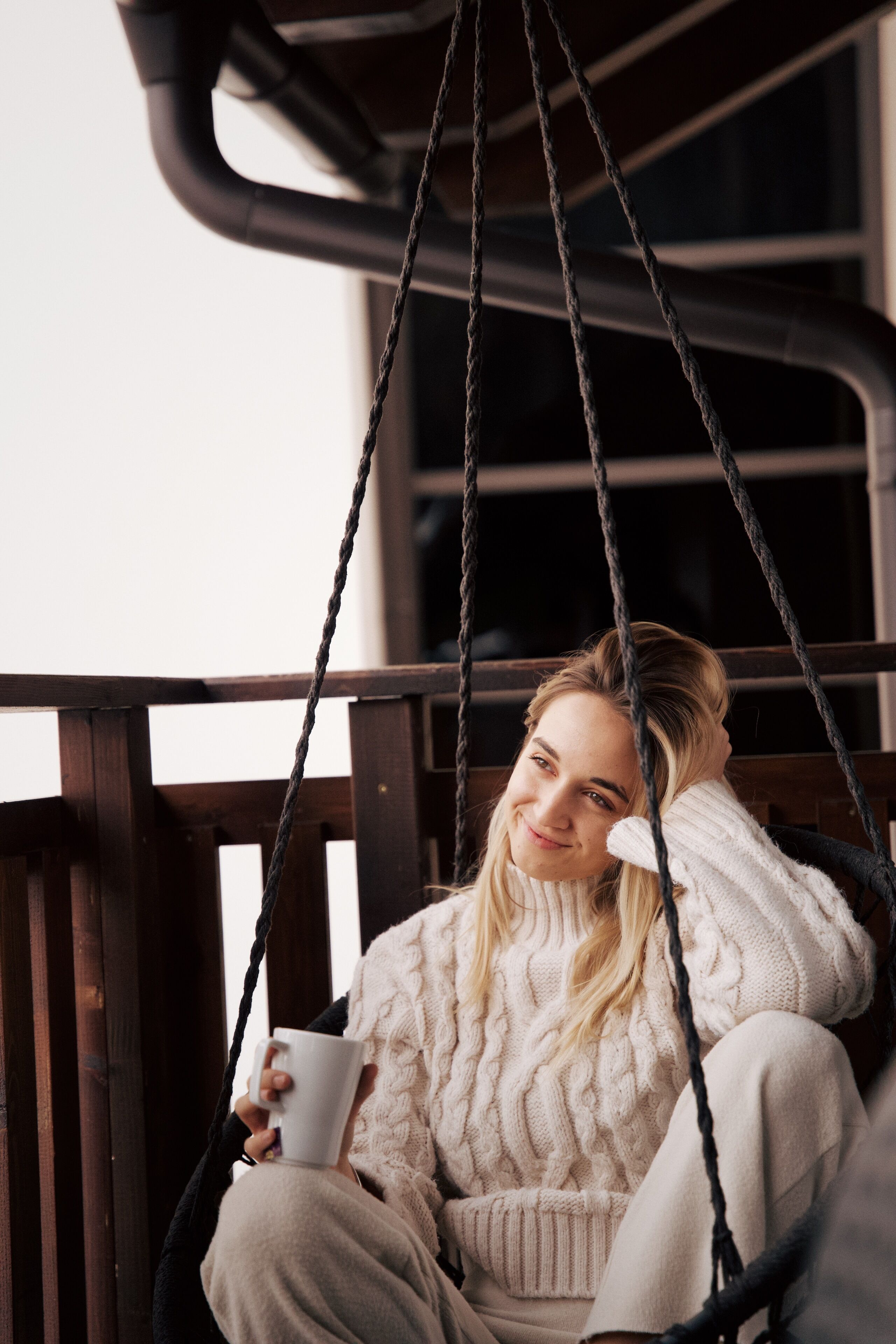 A person sitting on a swing chair, holding a cup.