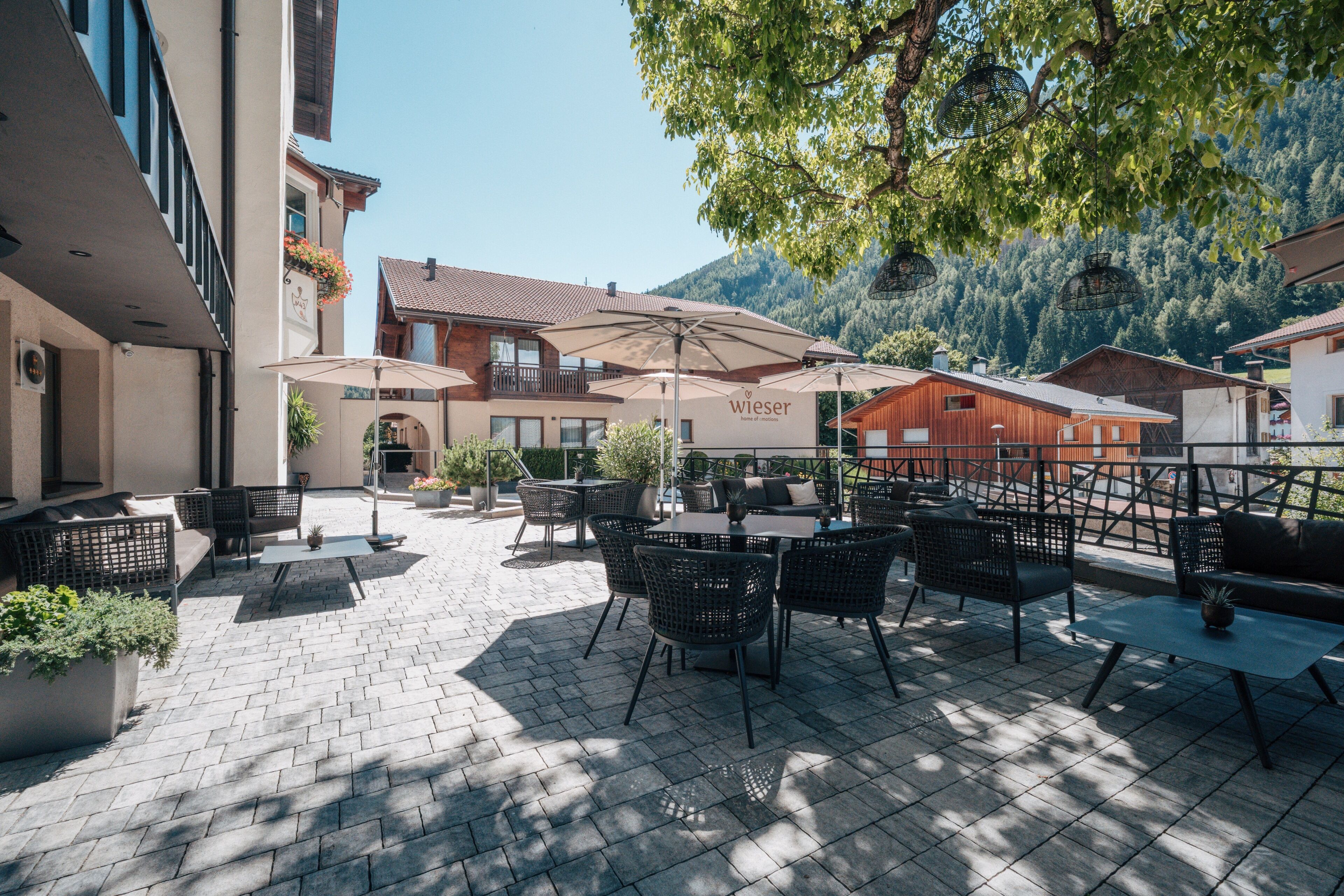 Un patio al aire libre con mesas y sillas, sombrillas y un edificio con un letrero que dice 'wieser' al fondo.