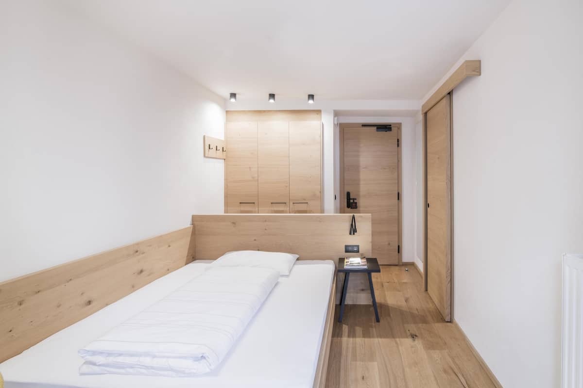 Een slaapkamer met een houten hoofdbord, een bed met witte beddengoed, een klein nachtkastje en een houten garderobe.