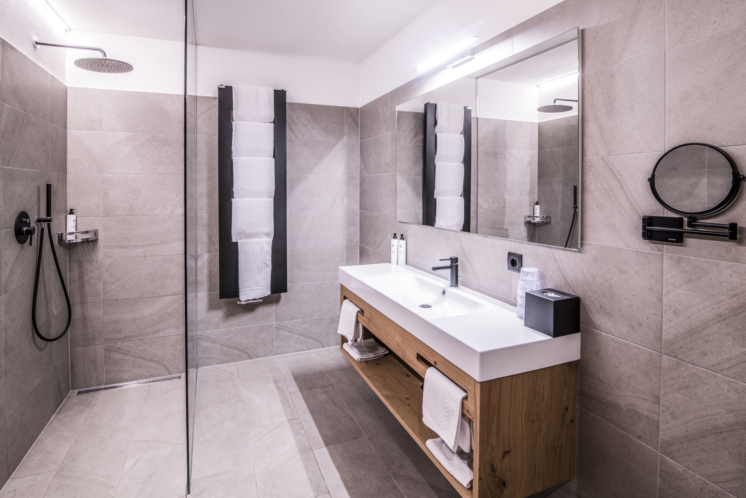 A modern bathroom with a glass-enclosed shower, a wooden vanity with a white sink, and a large mirror.