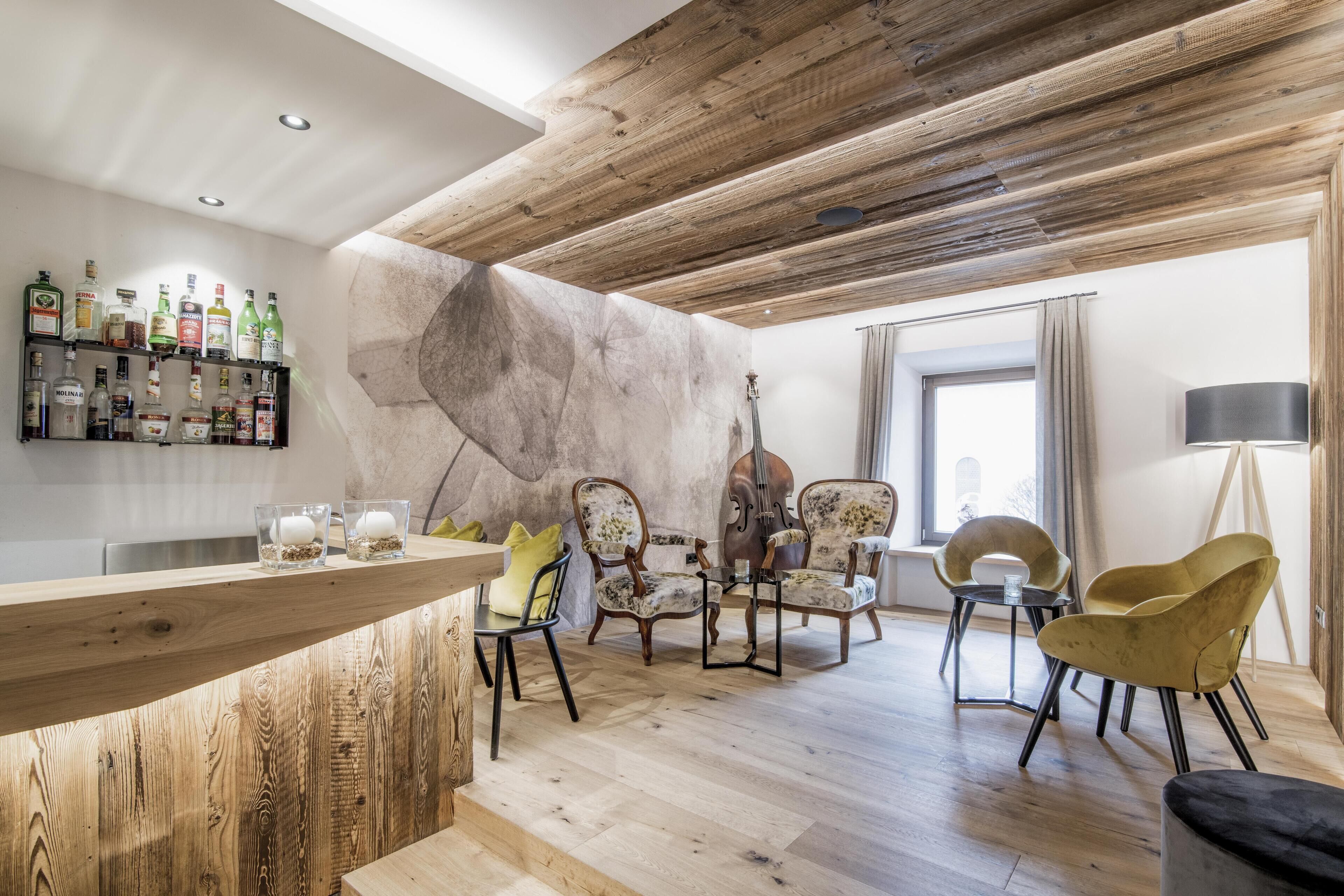 Una sala de estar moderna con techo de madera, una zona de bar con botellas de licor y un ventanal con cortinas.