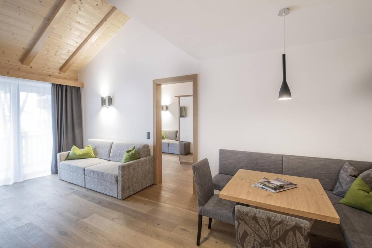 Een moderne woonkamer met een houten plafond, grijze banken, een houten salontafel en een hanglamp.