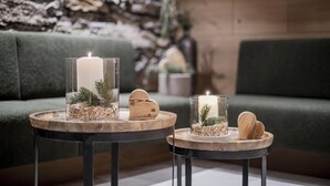 Two round tables with candles and wooden decorations, placed in front of a green sofa and a stone wall. - Hotel Wieser (Campo di Trens)
