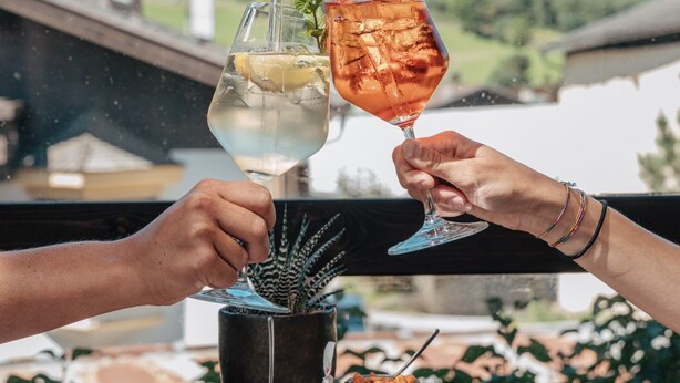 Two people toasting with drinks, a plate of snacks, and a view of mountains in the background. - Hotel Wieser (Campo di Trens)