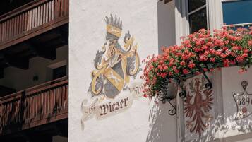 A building with a balcony, a window with a flower box, and a coat of arms on the wall.