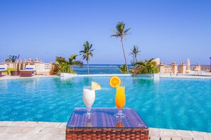 A poolside view with a clear view of the ocean, palm trees, and a table with two drinks.