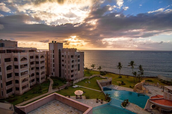 A hotel with a swimming pool, a view of the ocean, and a courtyard with palm trees.