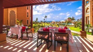 Un espacio exterior para comer con mesas dispuestas para los huéspedes, con vista a una piscina y un jardín ajardinado.