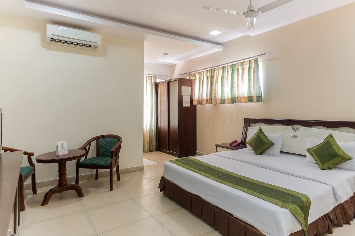 A hotel room with a bed, a chair, a small table, and an air conditioning unit.