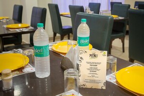 A hotel dining area with tables set for breakfast, including Bisleri water bottles, yellow plates, and a menu. - Treebo Sravya Residency, Hi-Tech Gachibowli (Hyderabad)