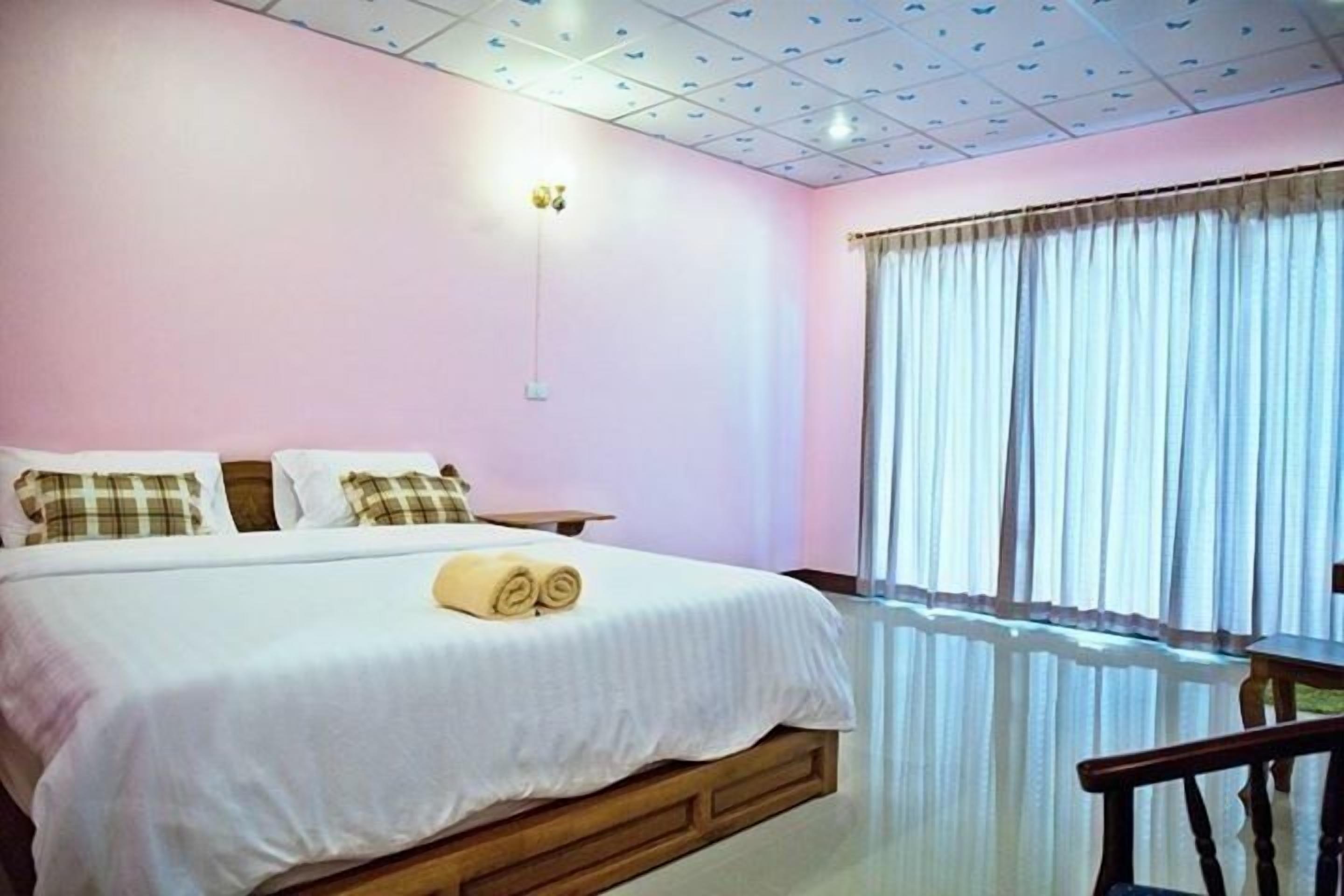 A bedroom with a bed, a bedside table, a chair, and a window with curtains.