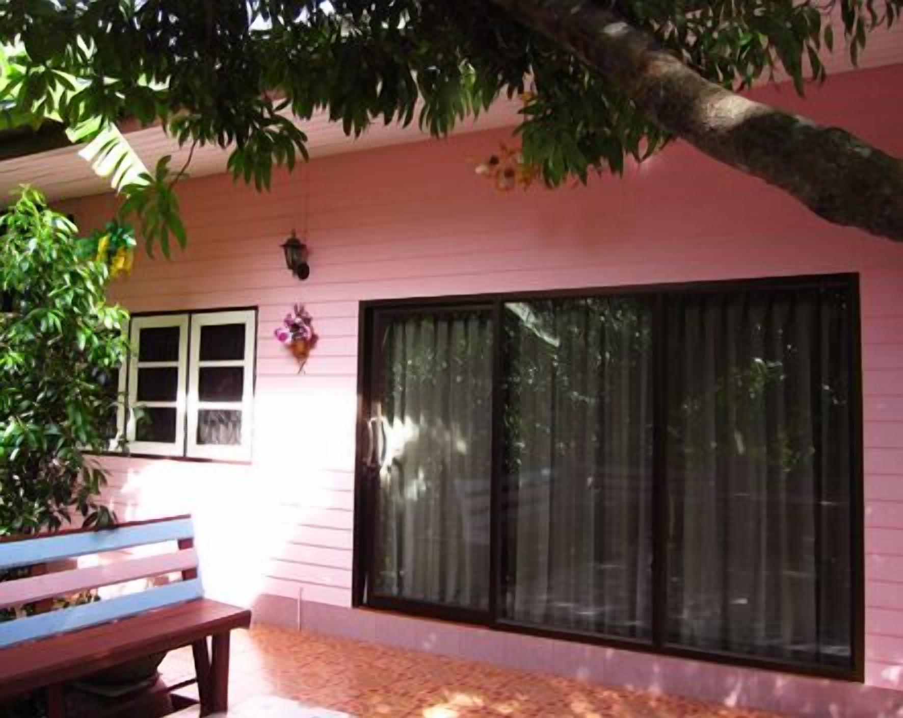 A pink house with a large window, a bench, and a tree.