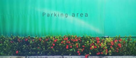 Un área de estacionamiento con un muro verde y flores rojas al frente.
