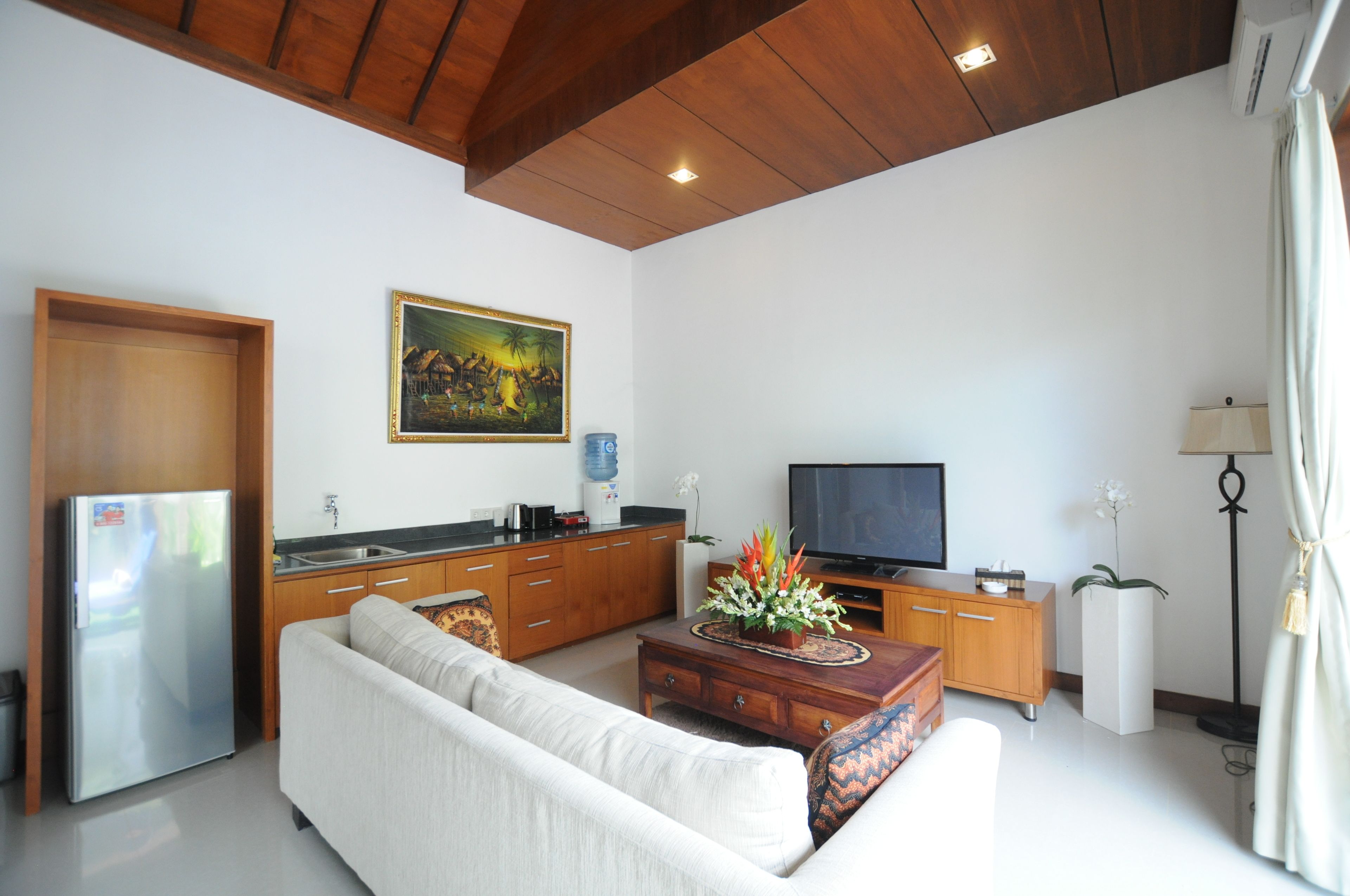 A modern living room with a sofa, coffee table, TV, kitchen area, and artwork on the wall.