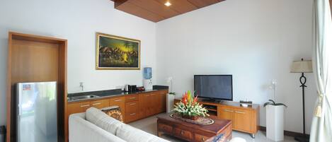 A modern living room with a sofa, coffee table, TV, kitchen area, and artwork on the wall.