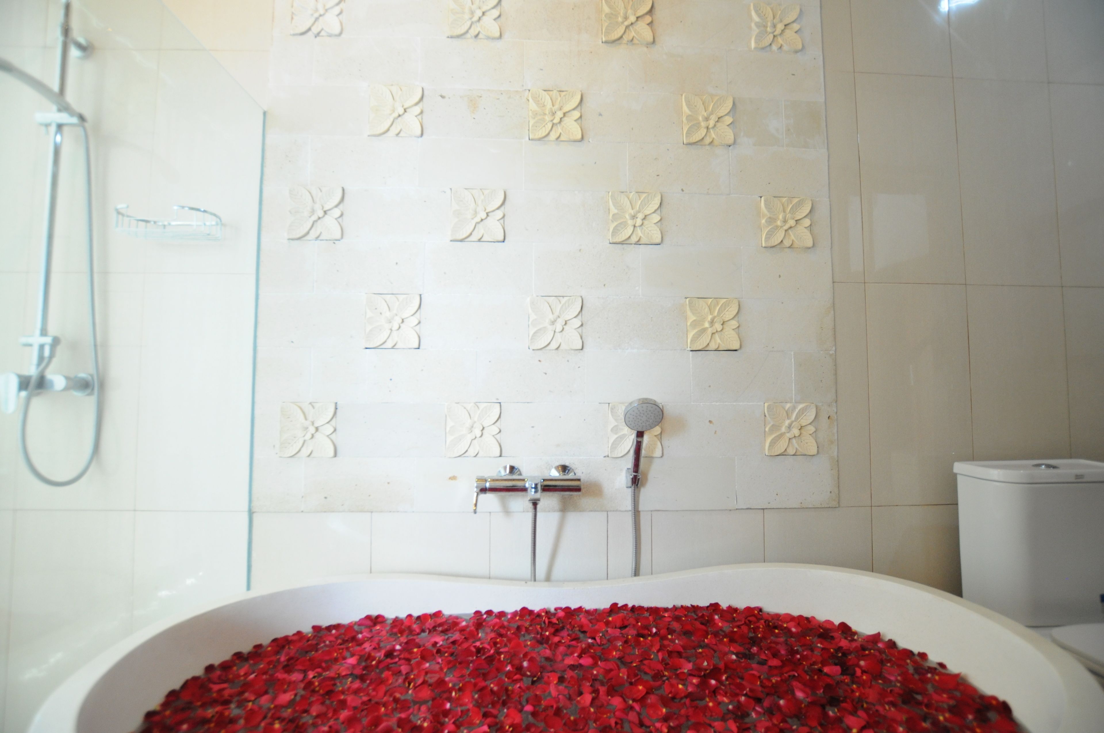 A bathroom with a bathtub filled with rose petals, a shower, and a toilet.