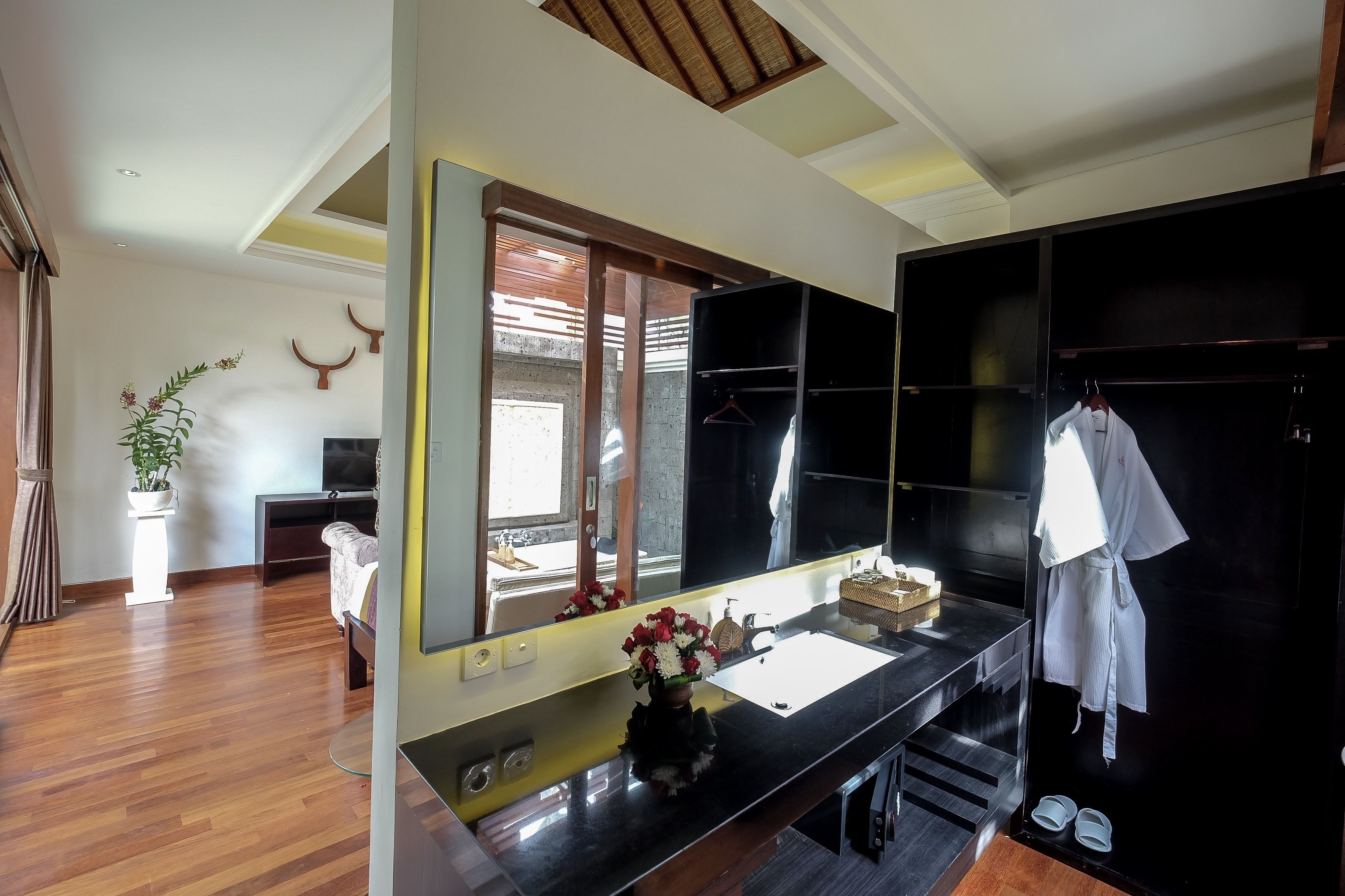 A modern bathroom with a large mirror, wooden flooring, a black vanity, and a towel rack.