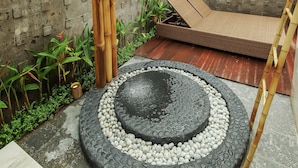 Un espace de détente extérieur moderne, agrémenté d’un élément décoratif aquatique en bambou, d’un espace de repos circulaire en pierre et d’une terrasse en bois.