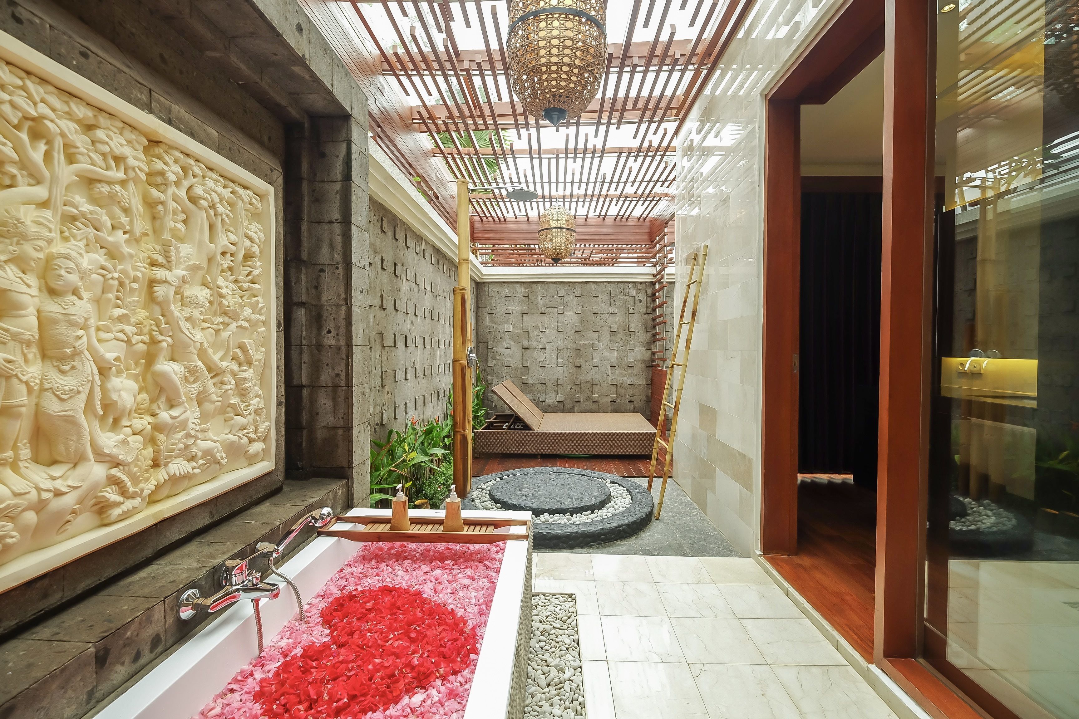 A bathroom with a bathtub filled with red flowers, a decorative wall with carvings, and a ceiling with a wooden lattice design.