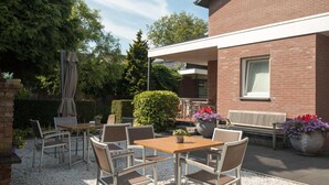 An outdoor patio area with a table and chairs, a bench, and potted plants. - Hotel Edenpark (Brunssum)