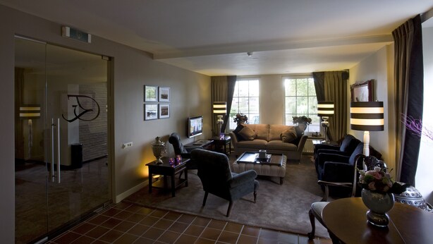 A modern living room with a glass partition, a sofa, a coffee table, and a TV. - Hotel Edenpark (Brunssum)