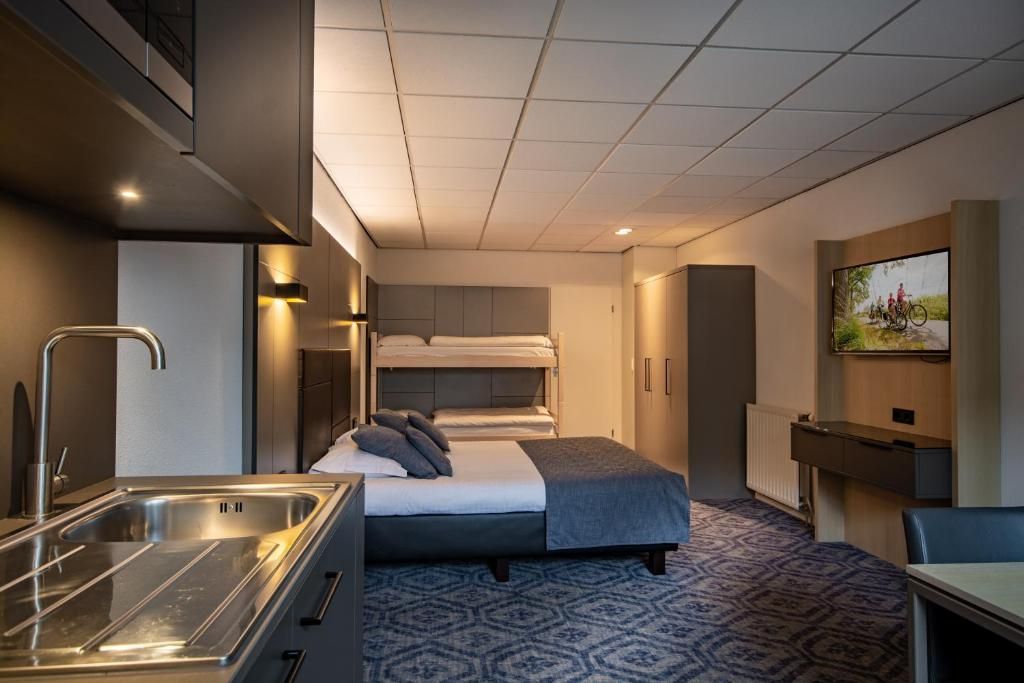 A compact hotel room with a bunk bed, a kitchenette, a small desk, and a television.