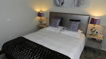 A neatly made bed with white linens and a dark brown throw blanket, flanked by two bedside tables with lamps and a wall-mounted artwork above.