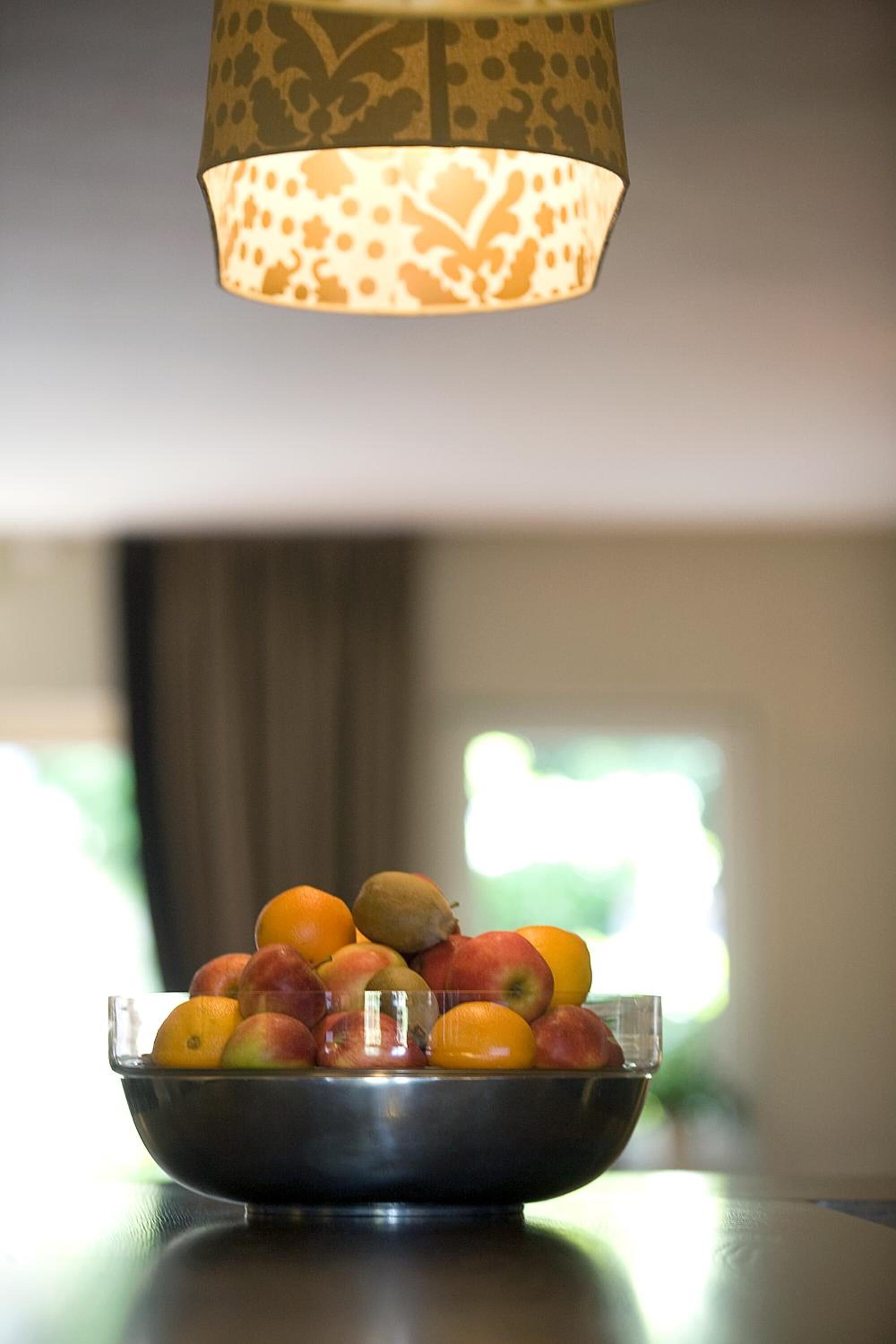 Eine Schale mit Obst auf einem Tisch unter einer Lampenschirm mit Muster.