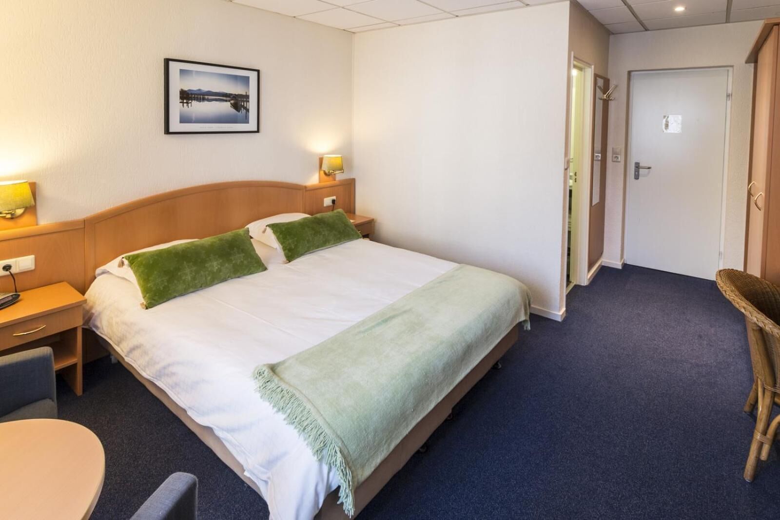 Une chambre d’hôtel avec un lit, des tables de chevet, une chaise, un bureau et un tableau au mur.
