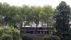 A two-story building with a brick facade, surrounded by lush greenery and a pond. - Hotel Edenpark (Brunssum)