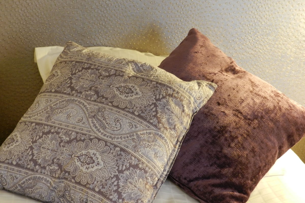 A bed with a patterned pillow and a solid brown pillow.