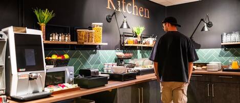 A modern kitchen with a 'Kitchen' sign, equipped with a coffee machine, toaster, and various food containers.