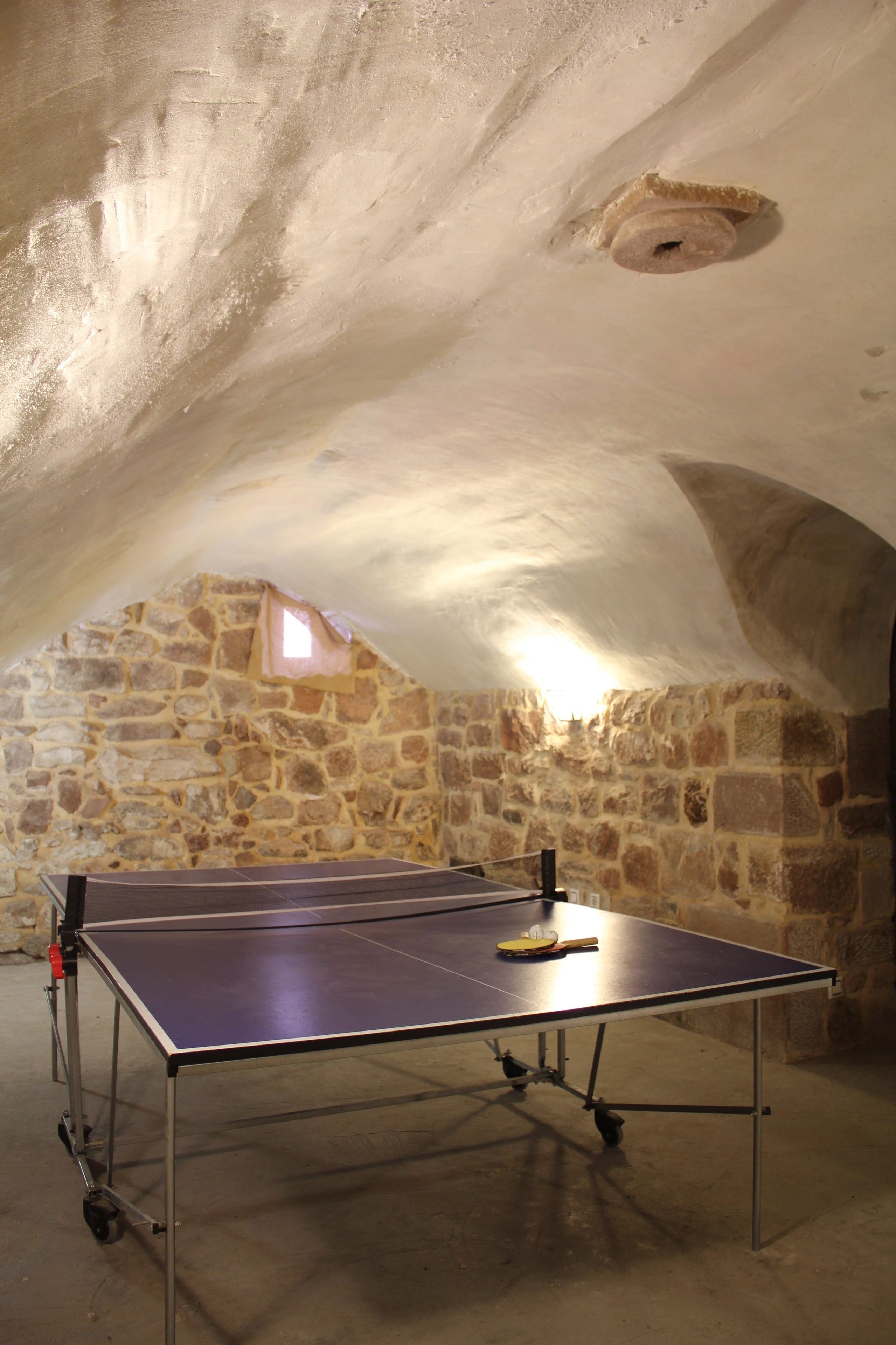 A ping pong table in a stone-walled room with a sloped ceiling.