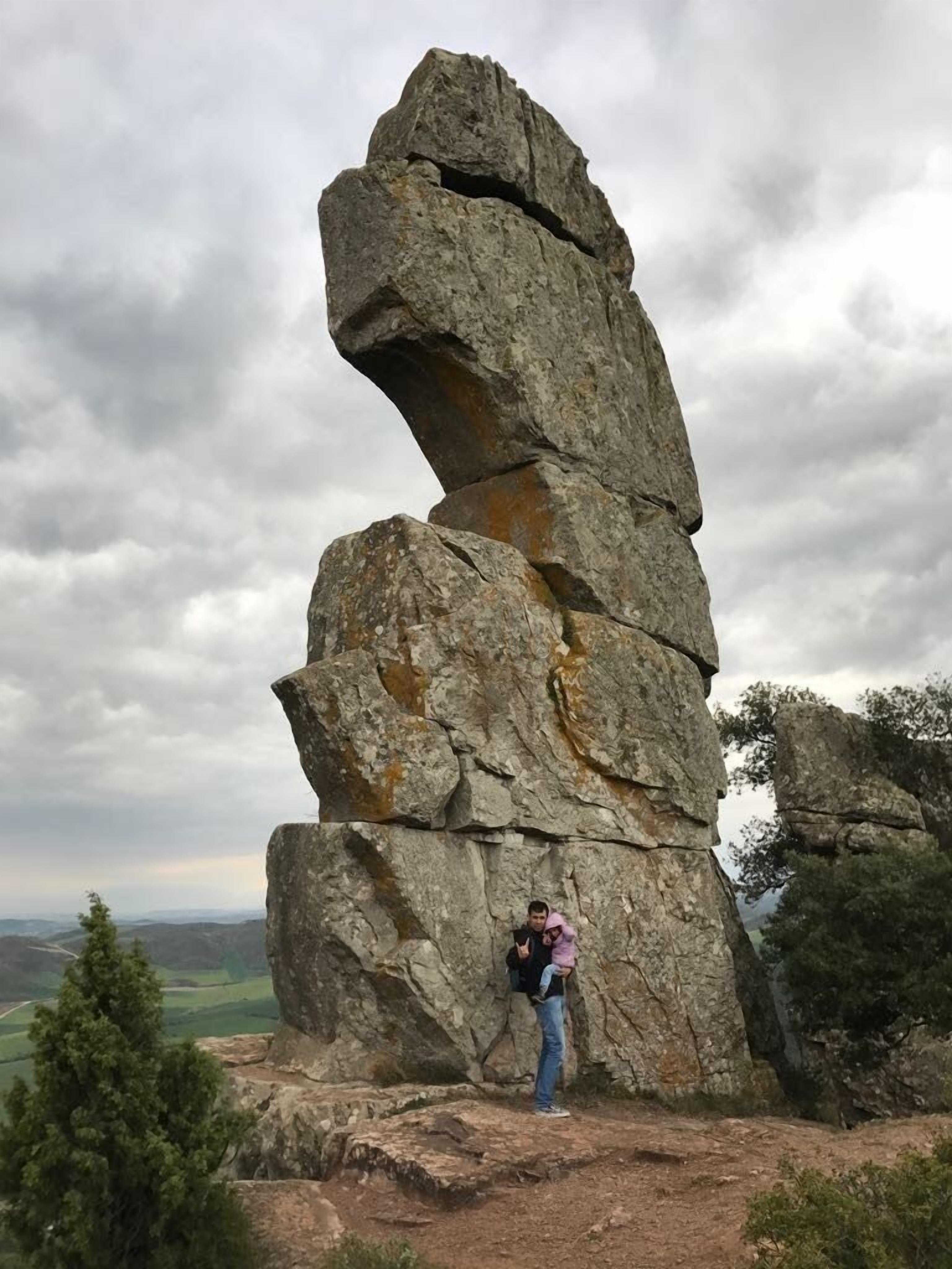 A person standing next to a large rock formation with a clear view of the surrounding landscape.