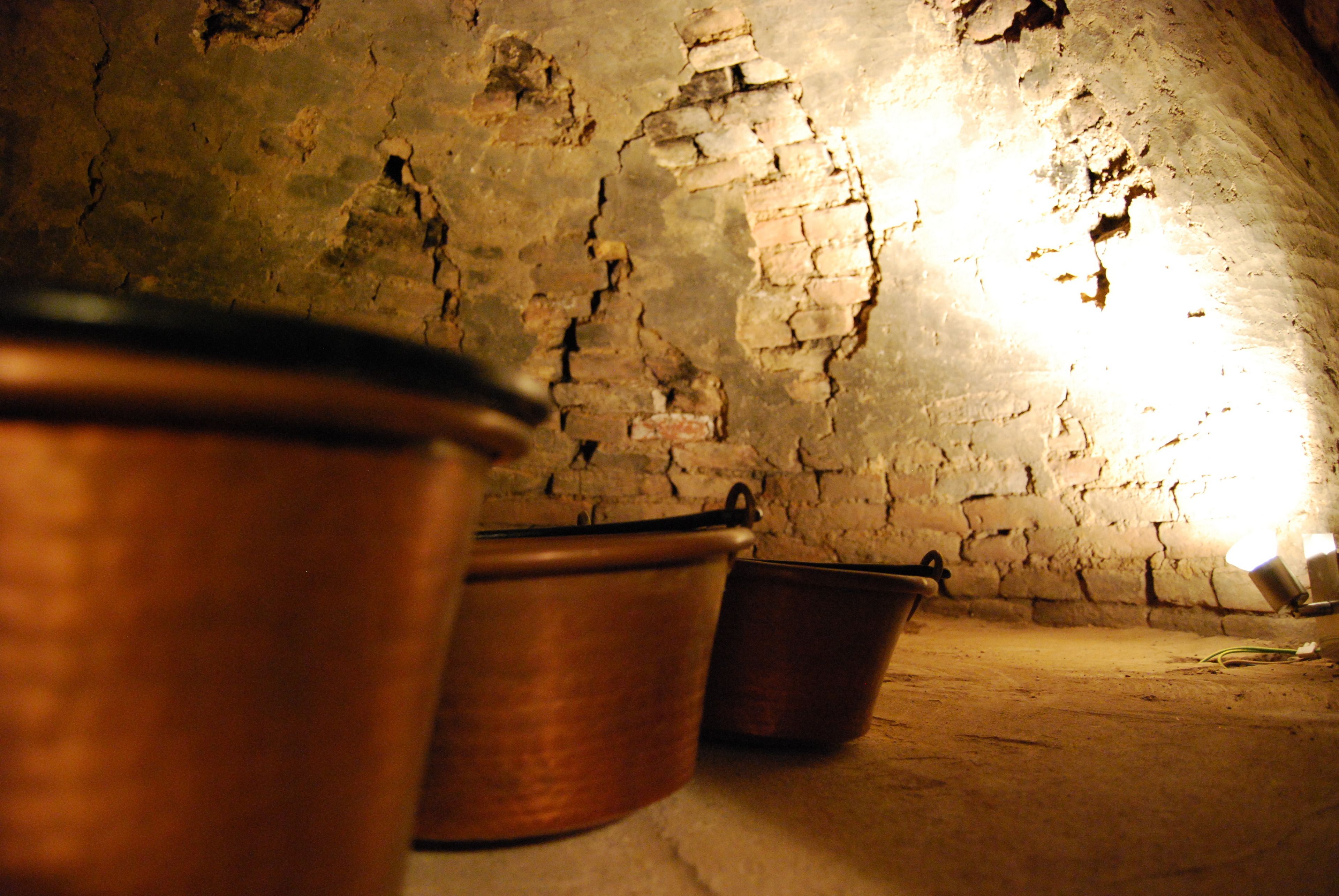 A rustic interior with exposed brick walls and three copper pots lined up against the wall.
