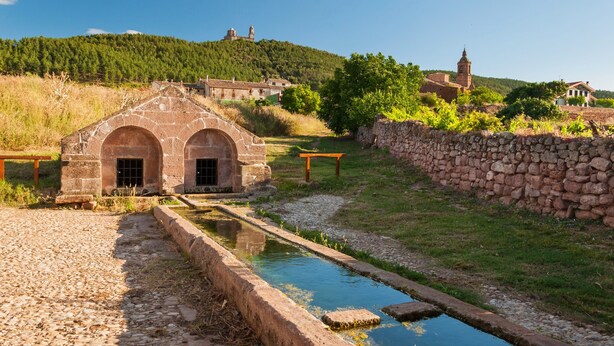 A stone building with arched doorways, a small pond, and a stone wall. - Hostal Rural Ioar (Sorlada)