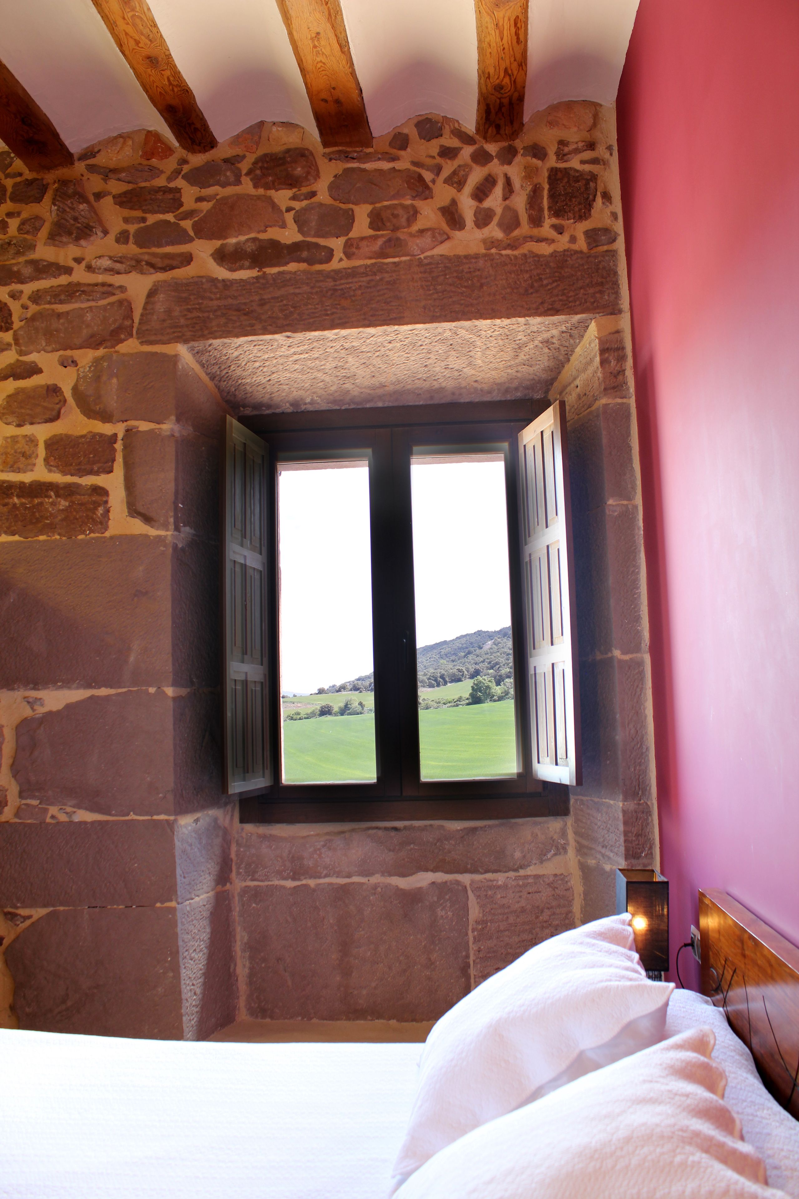 A bedroom with a stone wall, a window with shutters, and a bed with white linens.