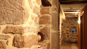 A stone-walled hallway with a wooden shelf and a stone wall with a small window. - Hostal Rural Ioar (Sorlada)