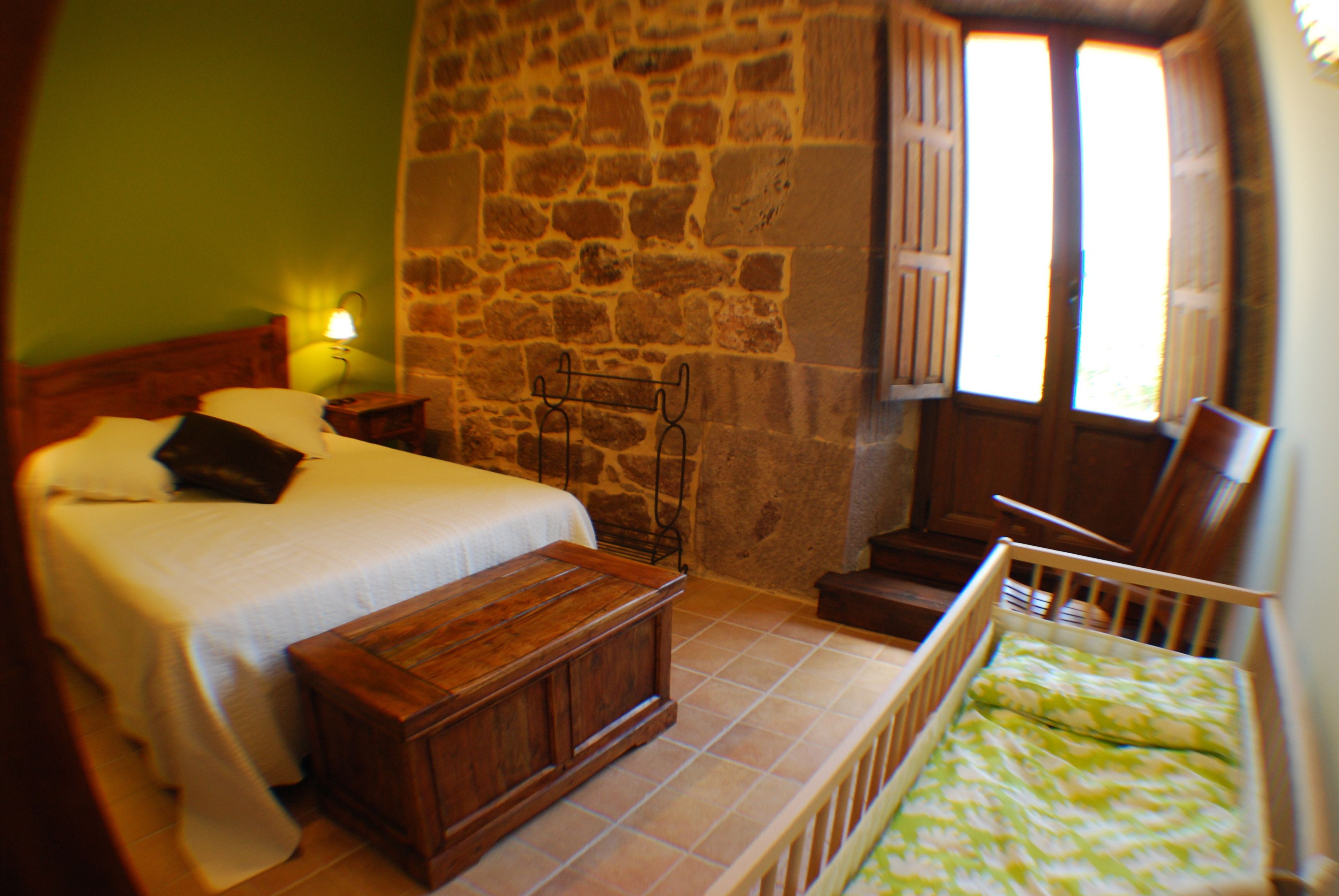 A bedroom with a bed, bedside table, wooden bench, and a crib.