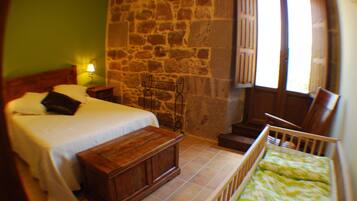 A bedroom with a bed, bedside table, wooden bench, and a crib.