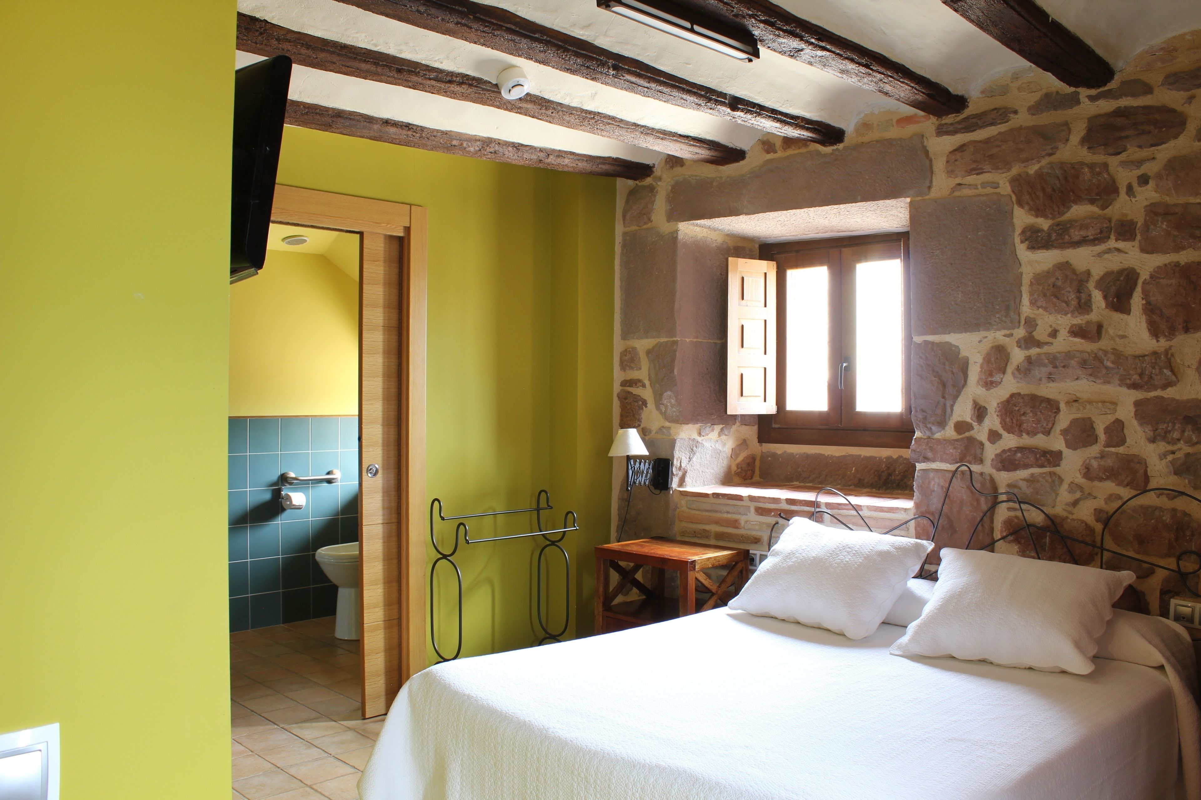 A bedroom with a bed, a wooden nightstand, a stone wall, and a window.