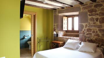 A bedroom with a bed, a wooden nightstand, a stone wall, and a window.