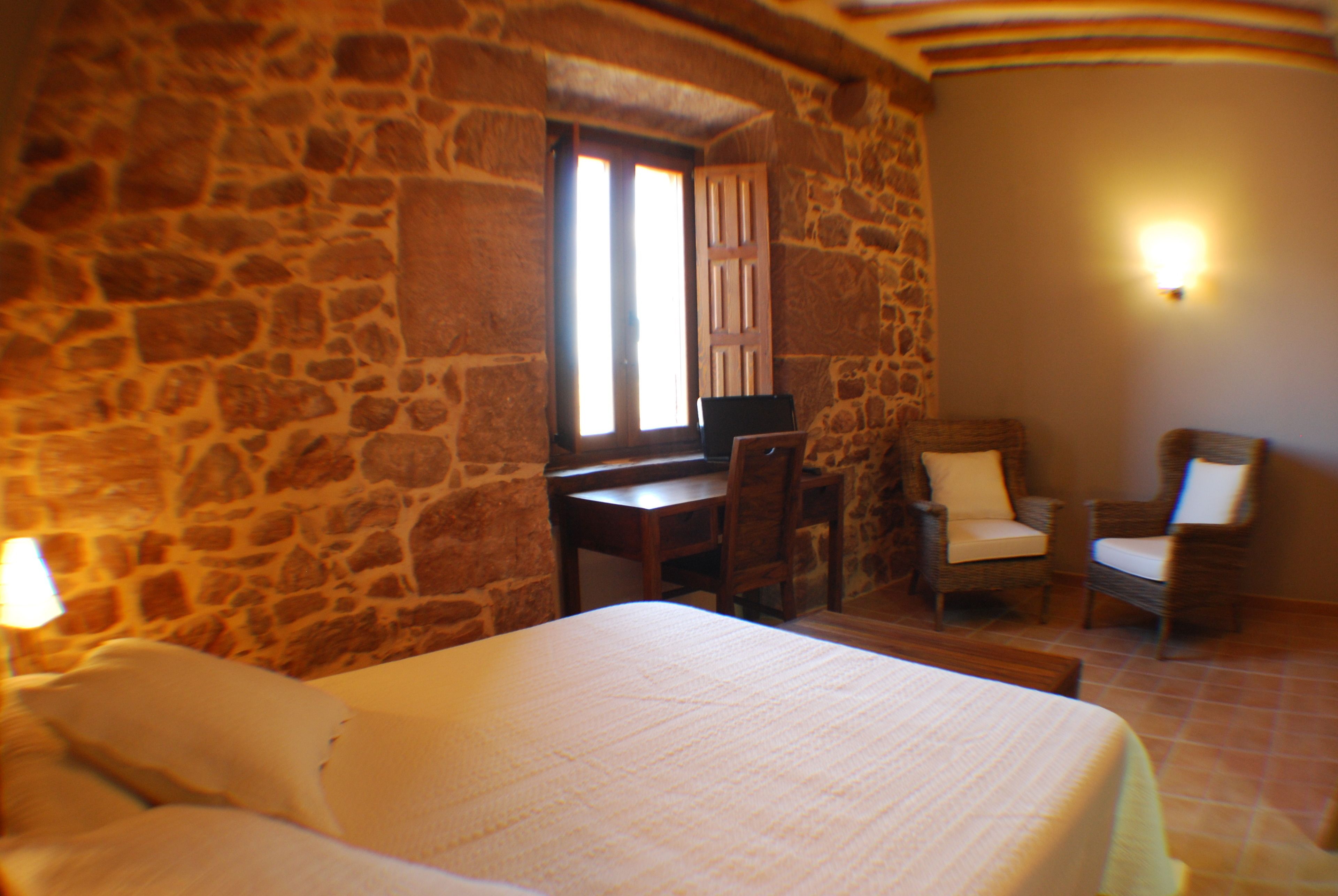 Una habitación con pared de piedra, una cama, un escritorio y dos sillas.