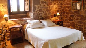 A bedroom with a stone wall, a wooden bed, two bedside tables, and a window with shutters. - Hostal Rural Ioar (Sorlada)