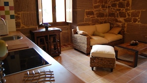 A kitchen with a stone wall, a wicker sofa, and a wooden table. - Hostal Rural Ioar (Sorlada)