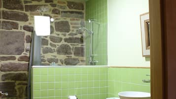 A bathroom with a stone wall, green tiles, a toilet, a sink, and a shower.