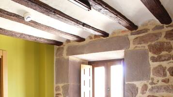 Un dormitorio con cama, mesita de noche de madera, pared de piedra y ventana con contraventanas de madera.