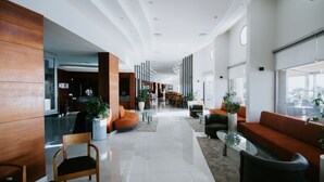 A modern hotel lobby with wooden paneling, a reception desk, seating areas, and large windows. - Faustina Hotel & Spa (Kusadasi)