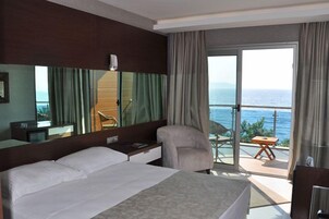 Camera d'albergo con letto, scrivania, sedia e balcone vista mare.