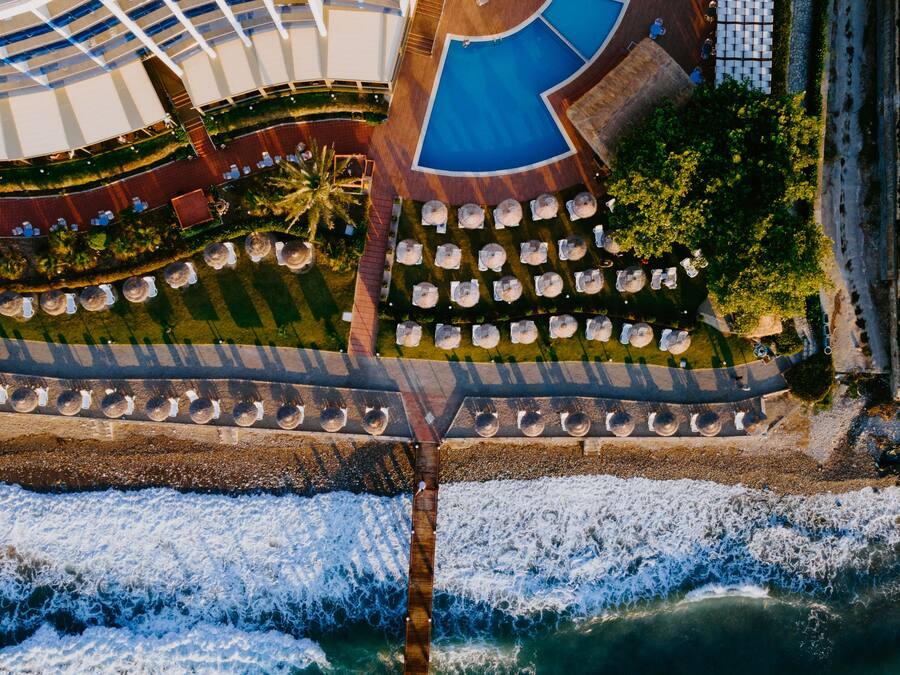 An aerial view of a cruise ship with a pool area, outdoor seating, and a pier extending into the water.